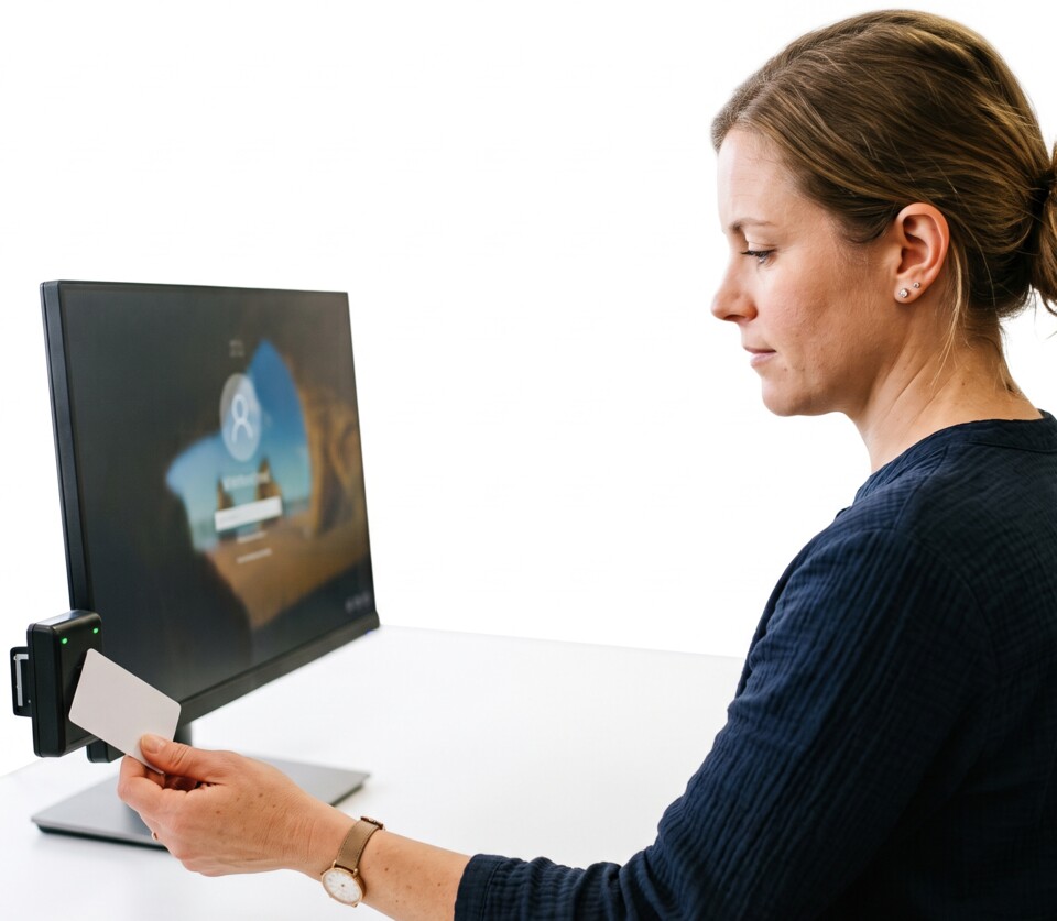 A receptionist at a small clinic tapping an access card against a reader next to a monitor to log into Windows